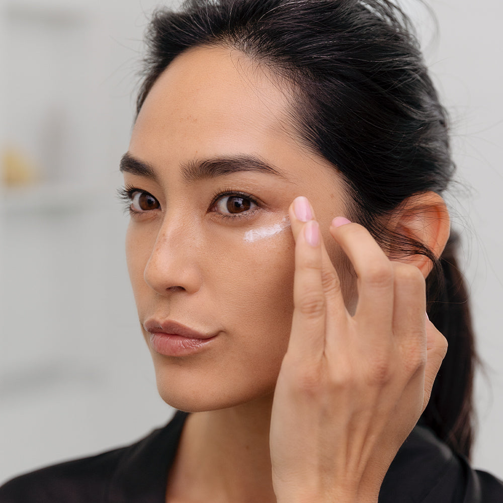 photo of woman gently applying eye cream to her left eye with the tip of her fourth finger