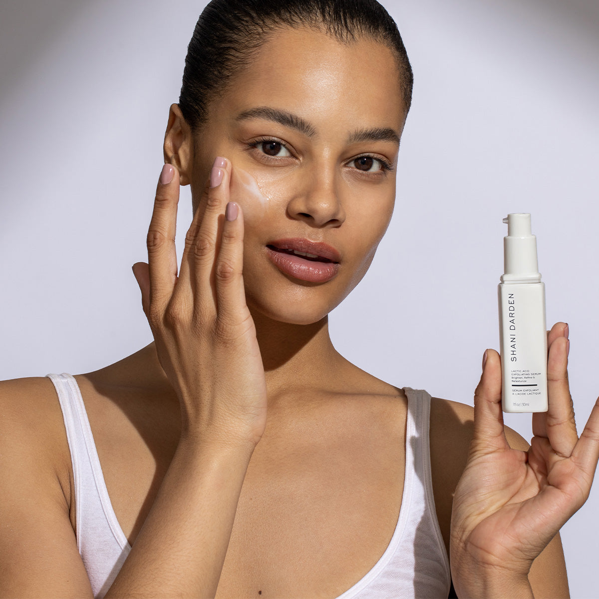 woman with her hair pulled back applying Lactic Acid Serum to her right cheek using a light touch of her finger tips