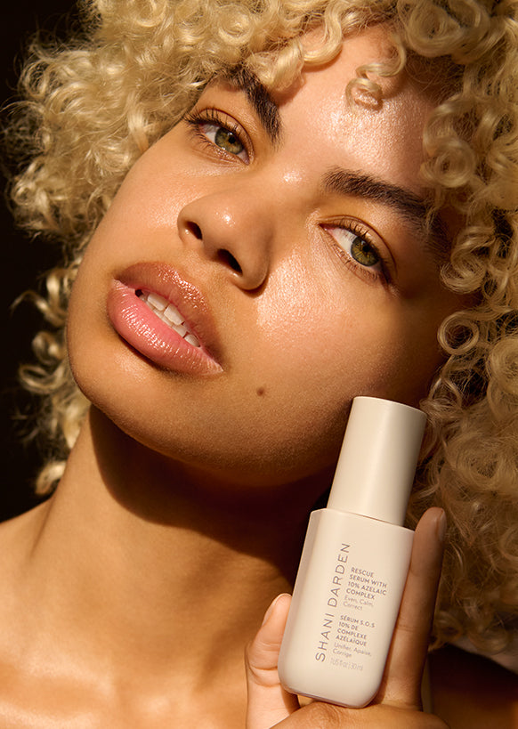 model with glowing skin holding shani darden rescue serum with 10% azelaic acid complex in natural sunlight