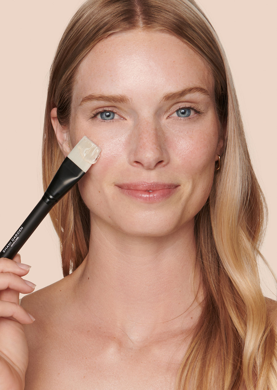 model applying shani darden triple acid signature peel with applicator brush on cheek